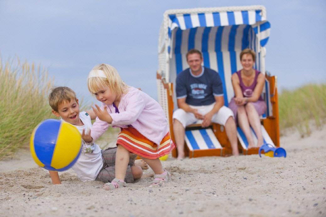 Eltern sitzen im Strandkorb und die Kinder spielen davor